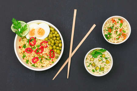 Beautiful Noodle Dish with Green Pea, Eggs, Red Hot Pepper and Greens with Chopsticks on Black Background. Instant Noodles - Top Viewの写真素材