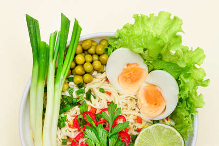 Beautiful Noodle Dish with Green Onions, Eggs, Green Pea, Red Hot Pepper, Greens and Lime on White Background. Instant Noodles with Vegetables - Top Viewの写真素材