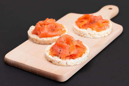 Tasty Rice Cake Sandwiches with Fresh Salmon Slices on Wooden Cutting Board. Easy Breakfast and Diet Food. Crispbread with Red Fish. Healthy Dietary Snackの写真素材