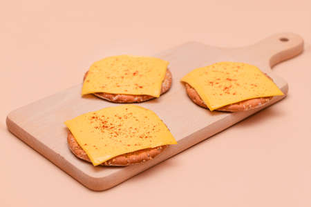Crispy Cracker Sandwiches with Cheese and Paprika on Wooden Cutting Board and Beige Background