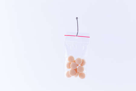 The Pharmaceutical Trap and Drug Addiction - Colored Pills or Tablets Hanging in Small Ziplock Bag on a Fishing Hook Against the White Backgroundの写真素材