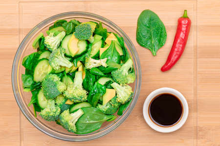 Fresh Green Salad of Avocado, Broccoli, Spinach and Cucumber with Soy Sauce and Red Hot Pepper on Wooden Cutting Board. Vegan Salad. Vegetarian Culture. Raw Food. Healthy Eating and Vegetable Dietの写真素材