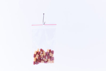 The Pharmaceutical Trap and Drug Addiction - Colored Pills or Tablets Hanging in Small Ziplock Bag on a Fishing Hook Against the White Backgroundの写真素材
