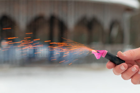 Burning Firecracker in a Hand. Guy Holding a Petard Outdoors in Winter at Daytime. Loud and Dangerous New Years Entertainment. Hooliganism with Pyrotechnics. Noise of Firecrackers in Public Placesの写真素材