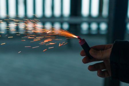 Burning Firecracker with Sparks. Guy Holding a Petard in a Hand. Loud and Dangerous New Years Entertainment. Hooliganism with Pyrotechnics. Noise of Firecrackers in Public Placesの写真素材