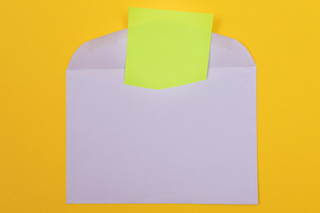 Violet Envelope with Blank Green Sheet of Paper Inside, Lying on Yellow Background - Mock Up with Copy Space. Receiving Mail or Notice, Sending Postcard - Top View, Flat Layの写真素材