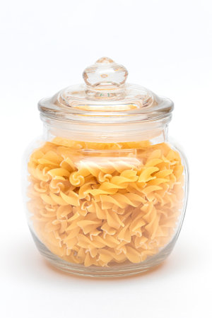 Uncooked Fusilli Pasta in Glass Jar on White Background. Raw and Dry Macaroni. Unhealthy and Fat Food. Italian Cultureの写真素材
