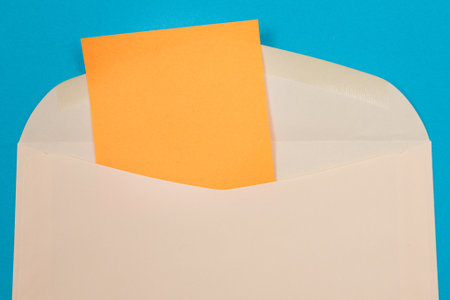 Beige Envelope with Blank Orange Sheet of Paper Inside, Lying on Blue Background - Mock Up with Copy Space. Receiving Mail or Notice, Sending Postcard - Top View, Flat Layの写真素材