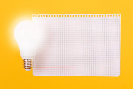 A Power Saving Lamp with Notepad Lying on Yellow Table, Blank Template with Copy Space - Top View, Flat Layの写真素材