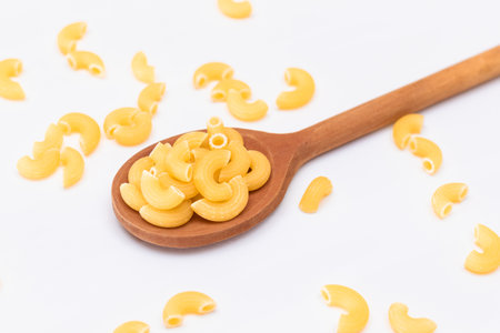 Uncooked Chifferi Rigati Pasta in Wooden Spoon on White Background. Fat and Unhealthy Food. Scattered Classic Dry Macaroni. Italian Culture and Cuisine. Raw Pastaの写真素材