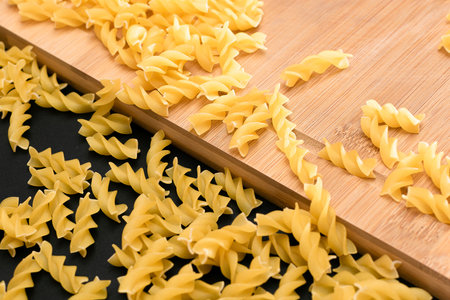 Uncooked Fusilli Pasta Scattered on Wooden Board and Black Table. Raw and Dry Macaroni. Fat and Unhealthy Foodの写真素材