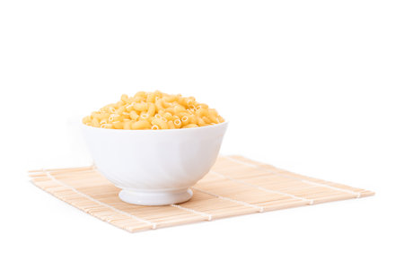 Uncooked Chifferi Rigati Pasta in White Cup on Bamboo Mat on White Background. Fat and Unhealthy Food. Scattered Classic Dry Macaroni. Italian Culture and Cuisine. Raw Pastaの写真素材