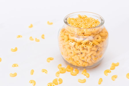 Uncooked Chifferi Rigati Pasta in Glass Jar on White Background. Fat and Unhealthy Food. Scattered Classic Dry Macaroni. Italian Culture and Cuisine. Raw Pastaの写真素材