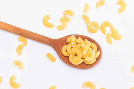 Uncooked Chifferi Rigati Pasta in Wooden Spoon on White Background. Fat and Unhealthy Food. Scattered Classic Dry Macaroni. Italian Culture and Cuisine. Raw Pastaの写真素材