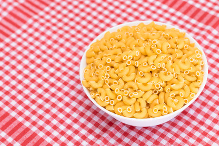 Uncooked Chifferi Rigati Pasta in White Cup on Red Checkered Towel. Fat and Unhealthy Food. Classic Dry Macaroni. Italian Culture and Cuisine. Raw Pastaの写真素材