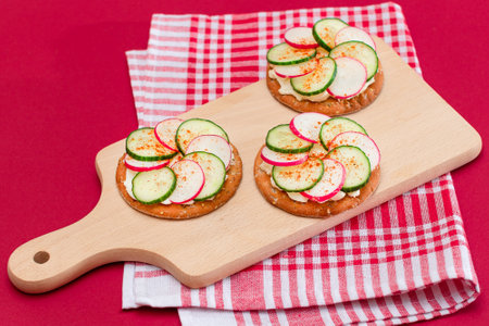 Light Breakfast or Diet Eating - Crispy Cracker Sandwich with Cream Cheese, Fresh Cucumber and Radish on Wooden Cooking Board on Magenta Backgroundの写真素材