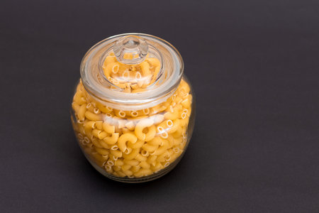 Uncooked Chifferi Rigati Pasta in Glass Jar on Black Background. Fat and Unhealthy Food. Classic Dry Macaroni. Italian Culture and Cuisine. Raw Pastaの写真素材