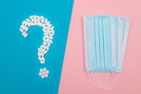 Question Mark Made from White Pills and Tablets with Medical Face Masks, Lying on Split Blue and Pink Background. Global Pharmaceutical Industry and Medicinal Productsの写真素材