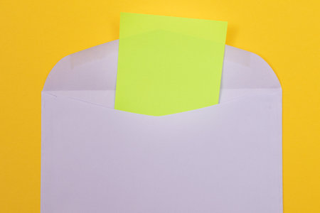 Violet Envelope with Blank Green Sheet of Paper Inside, Lying on Yellow Background - Mock Up with Copy Space. Receiving Mail or Notice, Sending Postcard - Top View, Flat Layの写真素材