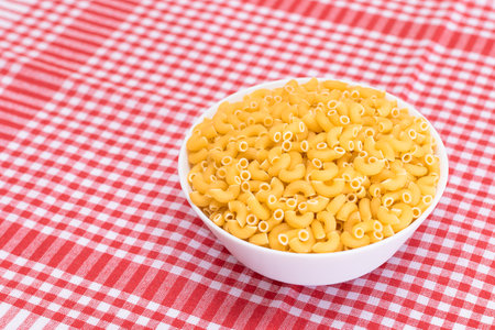 Uncooked Chifferi Rigati Pasta in White Cup on Red Checkered Towel. Fat and Unhealthy Food. Classic Dry Macaroni. Italian Culture and Cuisine. Raw Pastaの写真素材