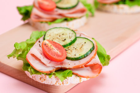Light Breakfast. Quick and Healthy Sandwiches. Rice Cakes with Ham, Tomato, Fresh Cucumber and Green Salad on Wooden Cutting Boardの写真素材