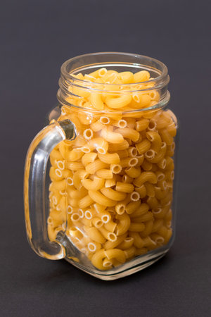 Uncooked Chifferi Rigati Pasta in Glass Jar on Black Background. Fat and Unhealthy Food. Classic Dry Macaroni. Italian Culture and Cuisine. Raw Pastaの写真素材