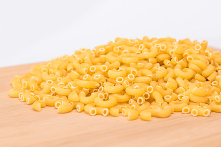 A Heap of Uncooked Chifferi Rigati Pasta on Wooden Kitchen Board. Fat and Unhealthy Food. Classic Dry Macaroni. Italian Culture and Cuisine. Raw Pastaの写真素材