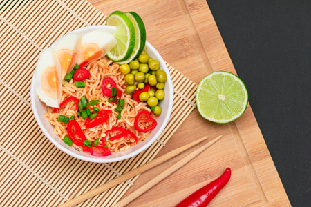 Beautiful Noodle Dish with Green Pea, Eggs, Red Hot Pepper, Greens and Lime with Chopsticks on Bamboo Cutting Board. Instant Noodlesの写真素材