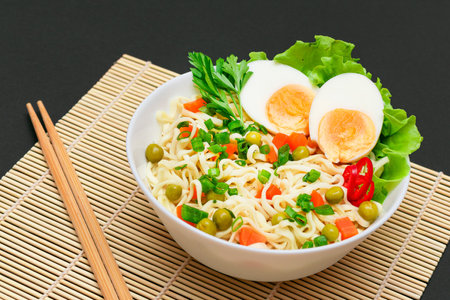 Beautiful Noodle Dish with Green Pea, Carrot, Eggs, Red Hot Pepper and Greens on Sushi Mat. Instant Noodles with Vegetablesの写真素材
