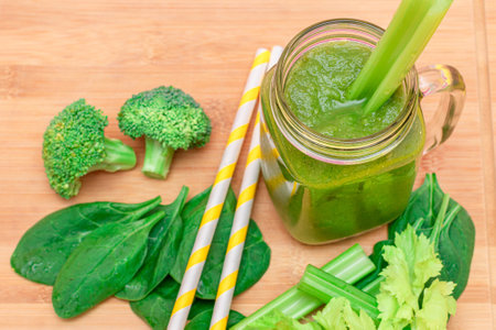 Fresh Green Smoothie of Apple, Celery, and Spinach in Glass Smoothie Jar with Yellow Cocktail Straw on Wooden Cutting Board. Vegan Detox Drink. Vegetarian Culture. Healthy Eating and Fruit Dietの写真素材