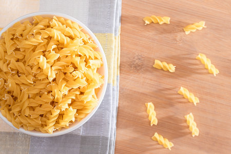 Uncooked Fusilli Pasta in White Bowl on Wooden Board. Raw and Dry Macaroni. Unhealthy and Fat Food. Italian Cultureの写真素材