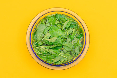 Fresh Baby Spinach Leaves in the Water in Glass Bowl on Yellow Background - Top View. Vegan and Vegetarian Culture. Raw Food, Green Leaves. Healthy Dietの写真素材