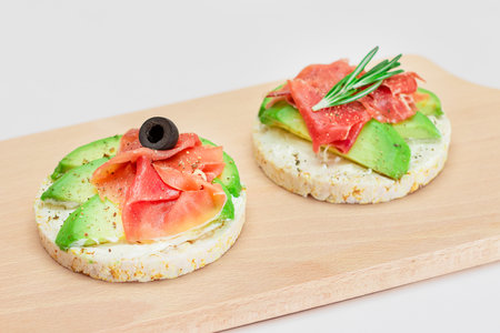 Rice Cake Sandwich with Avocado, Jamon, Olives and Rosemary on Wooden Cutting Board. Easy Breakfast. Quick and Healthy Sandwiches. Crispbread with Tasty Filling. Healthy Dietary Snackの写真素材