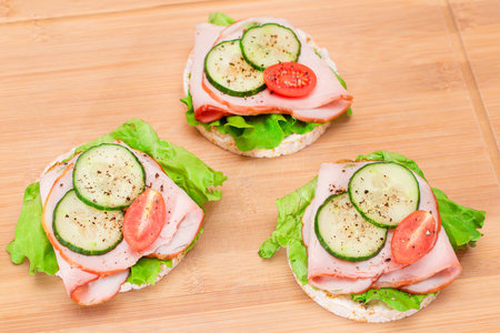Light Breakfast. Quick and Healthy Sandwiches. Rice Cakes with Ham, Tomato, Fresh Cucumber and Green Salad on Wooden Cutting Boardの写真素材
