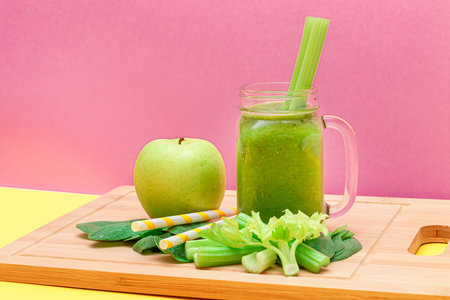 Fresh Green Smoothie of Apple, Celery, and Spinach in Glass Smoothie Jar with Yellow Cocktail Straw on Wooden Cutting Board. Vegan Detox Drink. Vegetarian Culture. Healthy Eating and Fruit Dietの写真素材