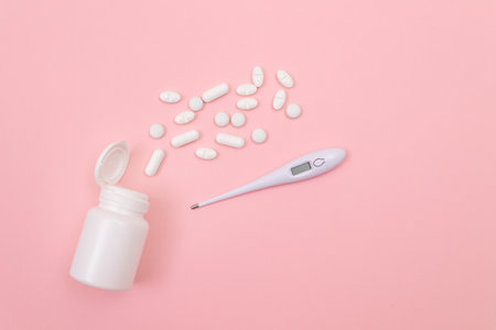 White Pills or Tablets with Electronic Thermometer on Pink Background. Pharmaceutical Industry and Medicinal Productsの写真素材