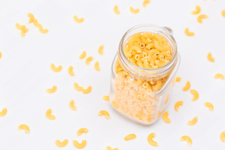 Uncooked Chifferi Rigati Pasta in Glass Jar on White Background. Fat and Unhealthy Food. Scattered Classic Dry Macaroni. Italian Culture and Cuisine. Raw Pastaの写真素材