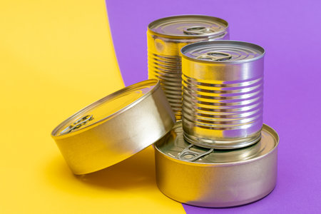A Group of Stacked Tin Cans with Blank Edges on Split Yellow and Violet Background. Canned Food. Different Aluminum Cans for Safe and Long Term Storage of Food. Steel Sealed Food Storage Containersの写真素材