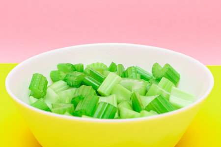 Fresh Chopped Celery Pieces with Water Drops in White Bowl on Yellow Background. Vegan and...