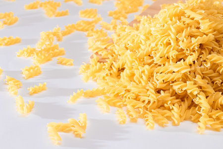 Uncooked Fusilli Pasta Scattered on Wooden Board and White Table. Raw and Dry Macaroni. Fat and Unhealthy Foodの写真素材