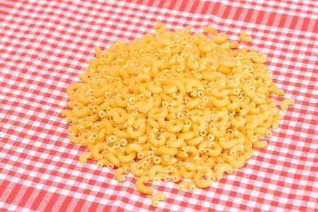 Scattered Uncooked Chifferi Rigati Pasta on Red Checkered Towel. Fat and Unhealthy Food. A Heap of Classic Dry Macaroni. Italian Culture and Cuisine. Raw Pastaの写真素材