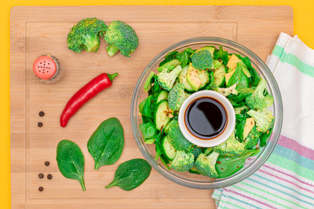 Fresh Green Salad of Avocado, Broccoli, Spinach and Cucumber with Soy Sauce and Red Hot Pepper on Wooden Cutting Board. Vegan Salad. Vegetarian Culture. Raw Food. Healthy Eating and Vegetable Dietの写真素材