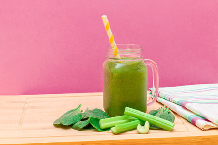 Fresh Green Smoothie of Apple, Celery, and Spinach in Glass Smoothie Jar with Yellow Cocktail Straw on Wooden Cutting Board. Vegan Detox Drink. Vegetarian Culture. Healthy Eating and Fruit Dietの写真素材