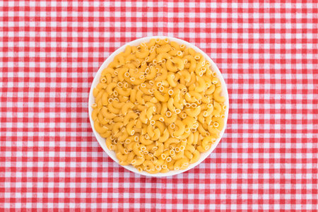 Uncooked Chifferi Rigati Pasta in White Cup on Red Checkered Towel. Fat and Unhealthy Food. Classic Dry Macaroni. Italian Culture and Cuisine. Raw Pastaの写真素材