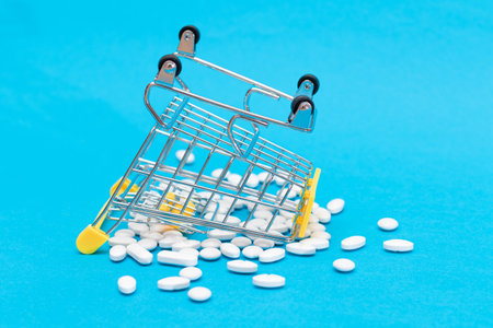 Buying Medicines. Expensive Medicine and Inflation: Scattered Pills or Capsules and Shopping Cart on Blue Background. Global Pharmaceutical Industry and Big Pharma. Ordering Pharmaceutical Productsの写真素材