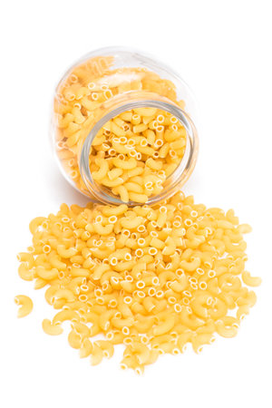 Uncooked Chifferi Rigati Pasta in Glass Jar Isolated on White Background. Fat and Unhealthy Food. Scattered Classic Dry Macaroni. Italian Culture and Cuisine. Raw Pastaの写真素材