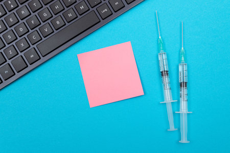 Vaccination, Immunology or Revaccination Concept - Two Medical Disposable Syringe Lying on Blue Table in Doctors Office in a Hospital or Clinic. Blank Pink Sticky Note - Mock Up with Copy Spaceの写真素材