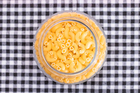 Uncooked Chifferi Rigati Pasta in Glass Jar on Black Checkered Towel. Fat and Unhealthy Food. Scattered Classic Dry Macaroni. Italian Culture and Cuisine. Raw Pastaの写真素材