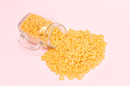 Uncooked Chifferi Rigati Pasta in Glass Jar on Pink Background. Fat and Unhealthy Food. Scattered Classic Dry Macaroni. Italian Culture and Cuisine. Raw Pastaの写真素材