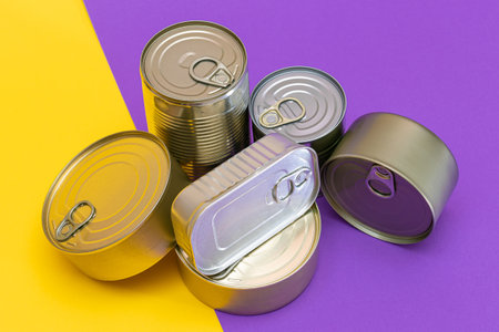 A Group of Stacked Tin Cans with Blank Edges on Split Yellow and Violet Background. Canned Food. Different Aluminum Cans for Safe and Long Term Storage of Food. Steel Sealed Food Storage Containersの写真素材